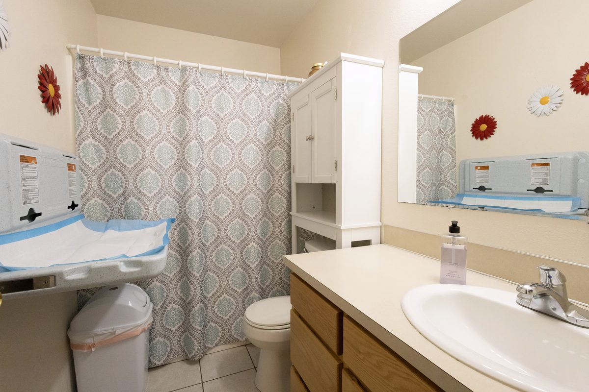 Restroom with a wall-mounted fold-down changing station and covered diaper pail