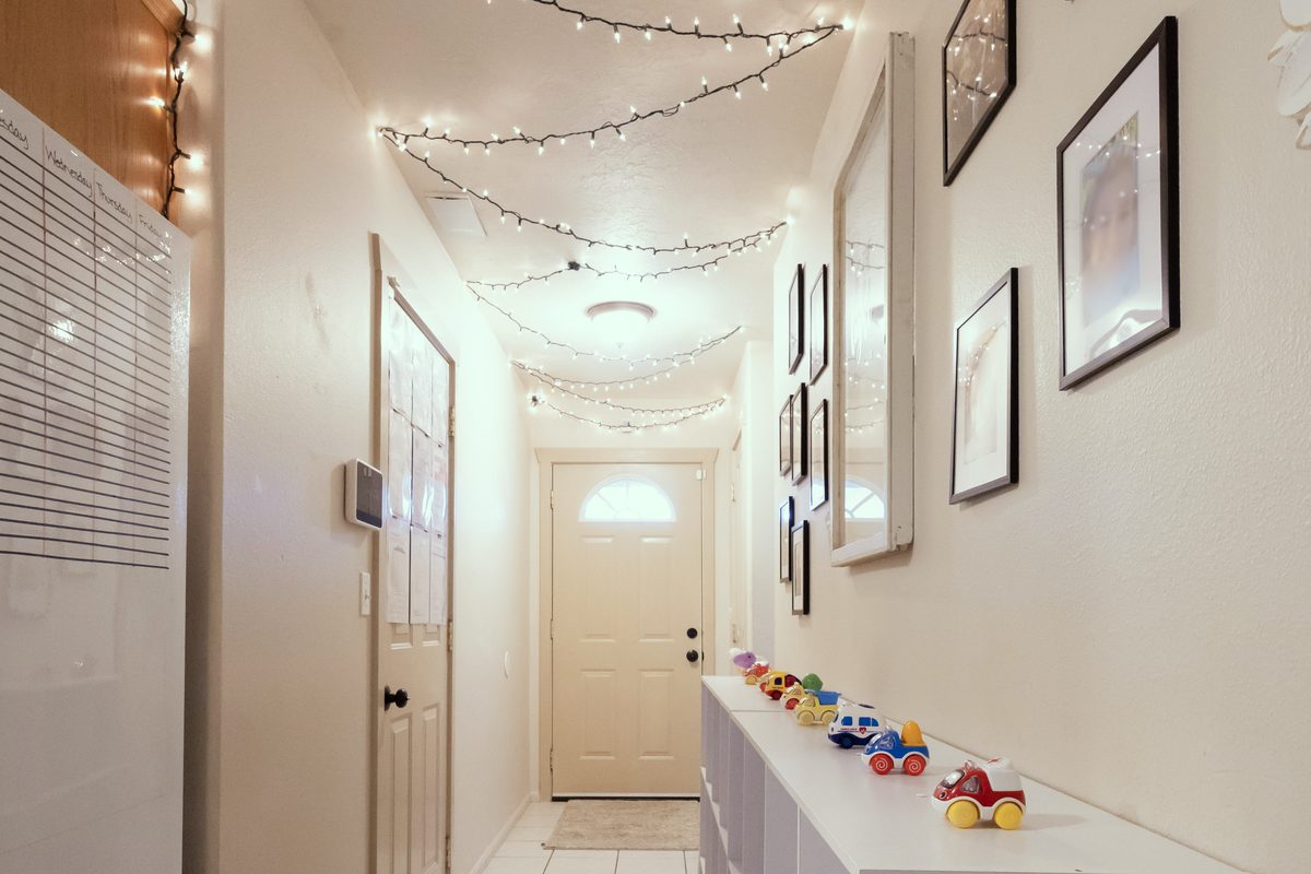 Entryway hallway with string lights, the front door, and a shelf of toy cars